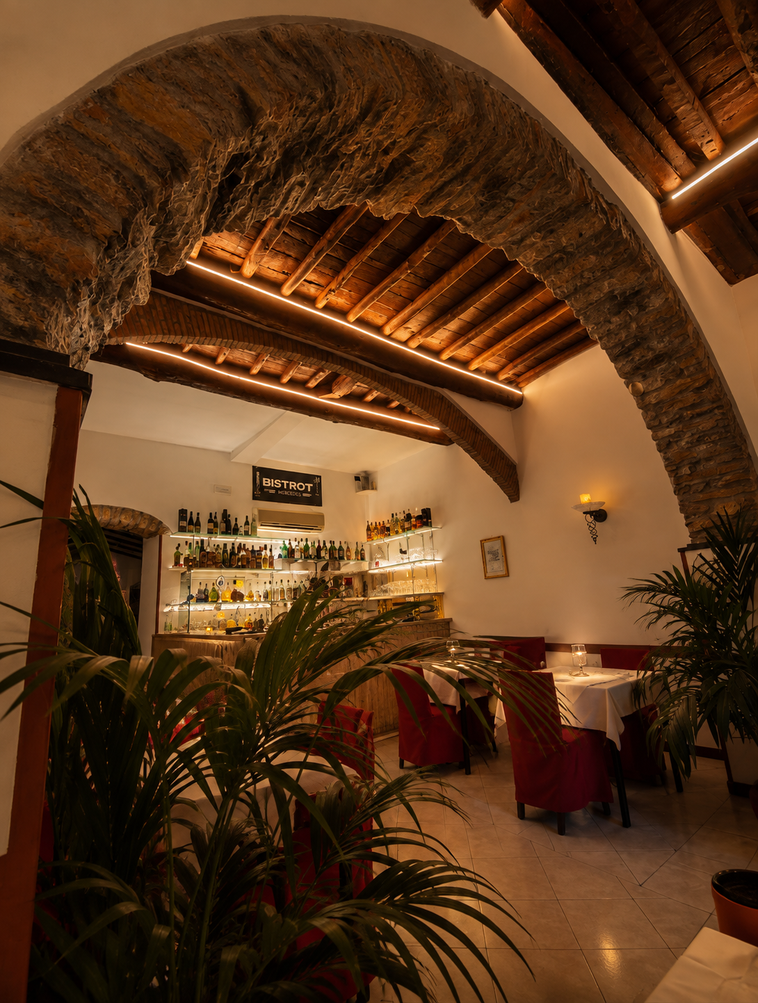 Sala con arco in pietra, travi in legno e tavoli apparecchiati del bistrot romantico di La Spezia